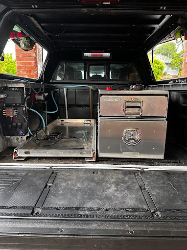 Pickup truck bed with metal sliding drawer system and stacked metal storage boxes under a canopy.